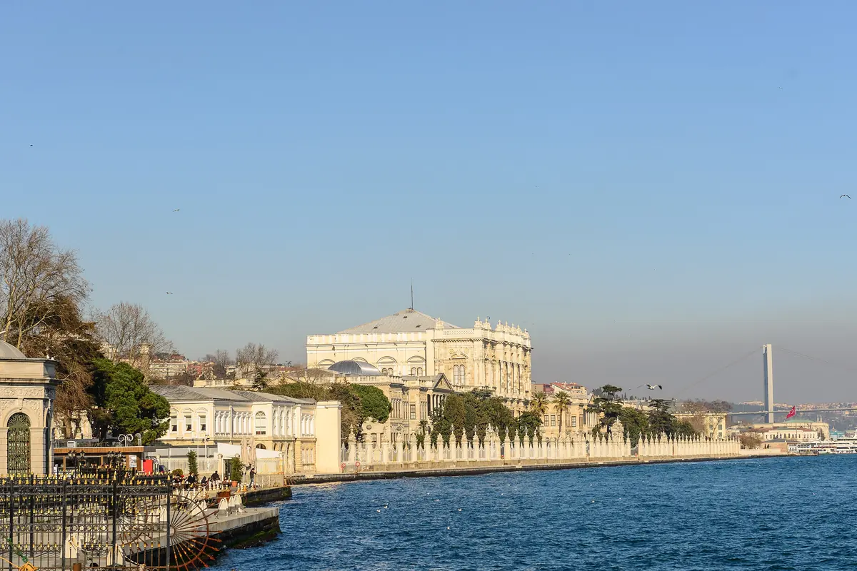 ボスポラス海峡沿いに建つDolmabahçe Palaceとその隣のモスク、遠景には橋、澄み渡る青空