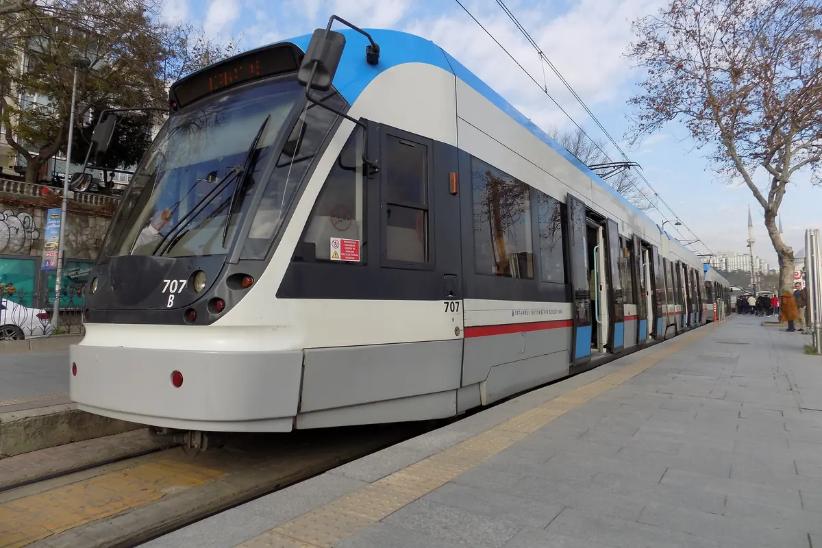 Šedobílá tramvaj T1 stojící na nástupišti v Kabataş v Istanbulu za jasného dne, vedle kolejí holé stromy
